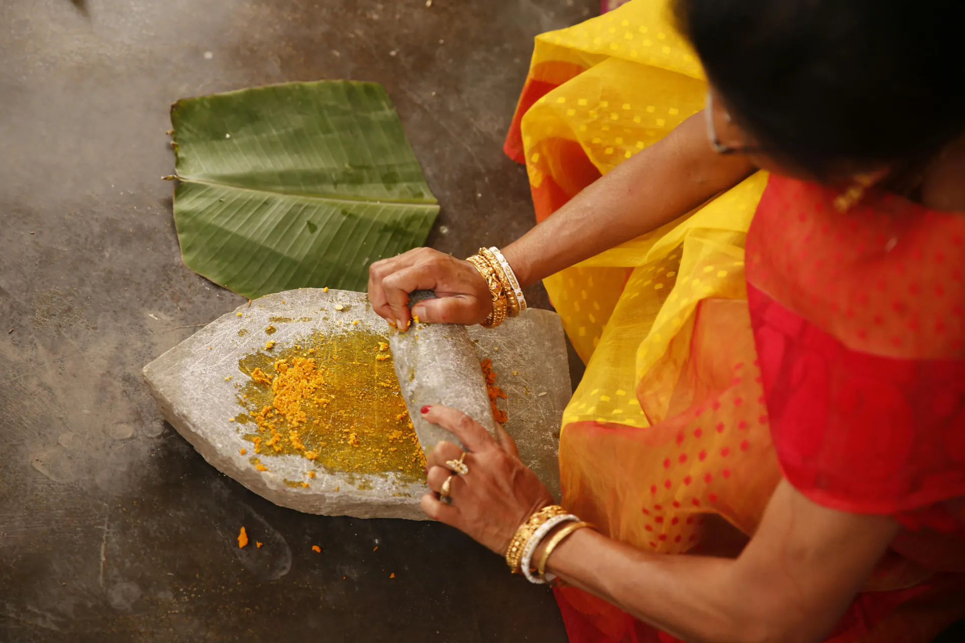 Woman in a traditional saree grinding fresh turmeric on a grinding stone