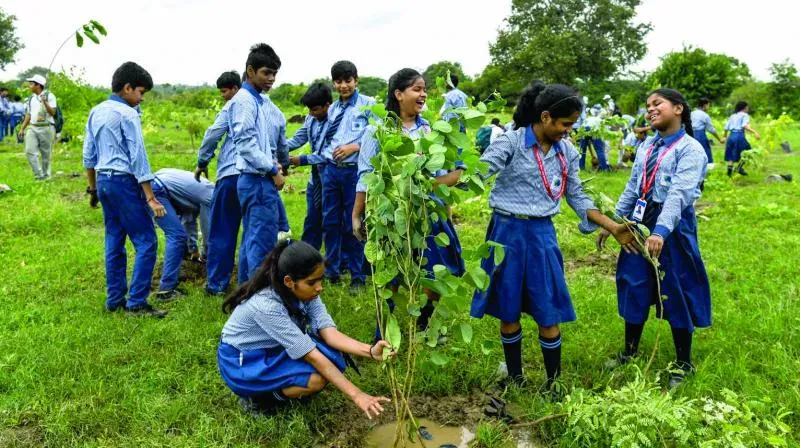 Students in uniform planting saplings during a tree plantation drive