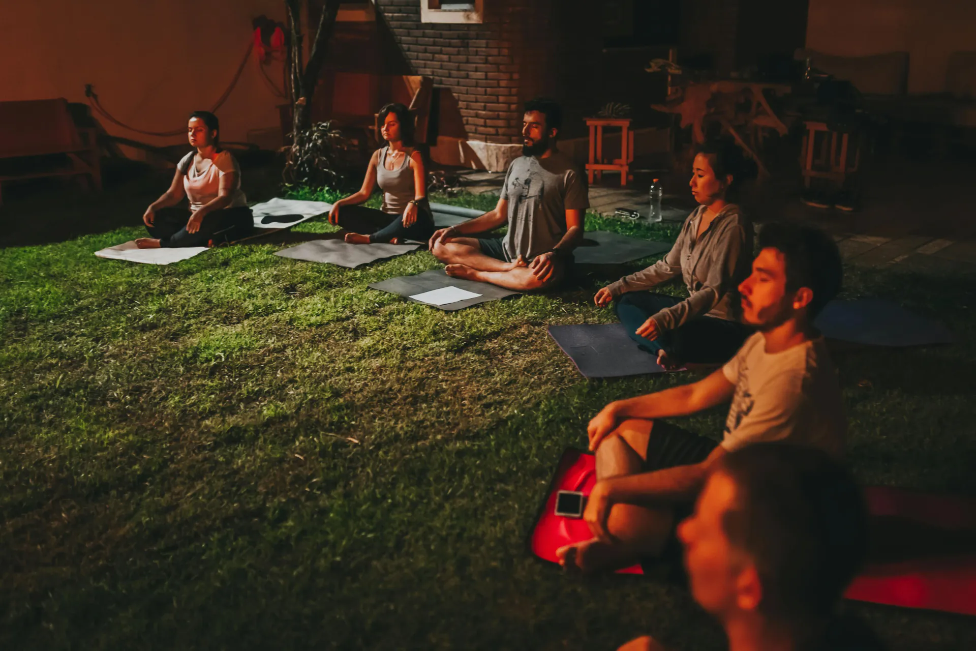 Group meditating outdoors on the grass at dusk
